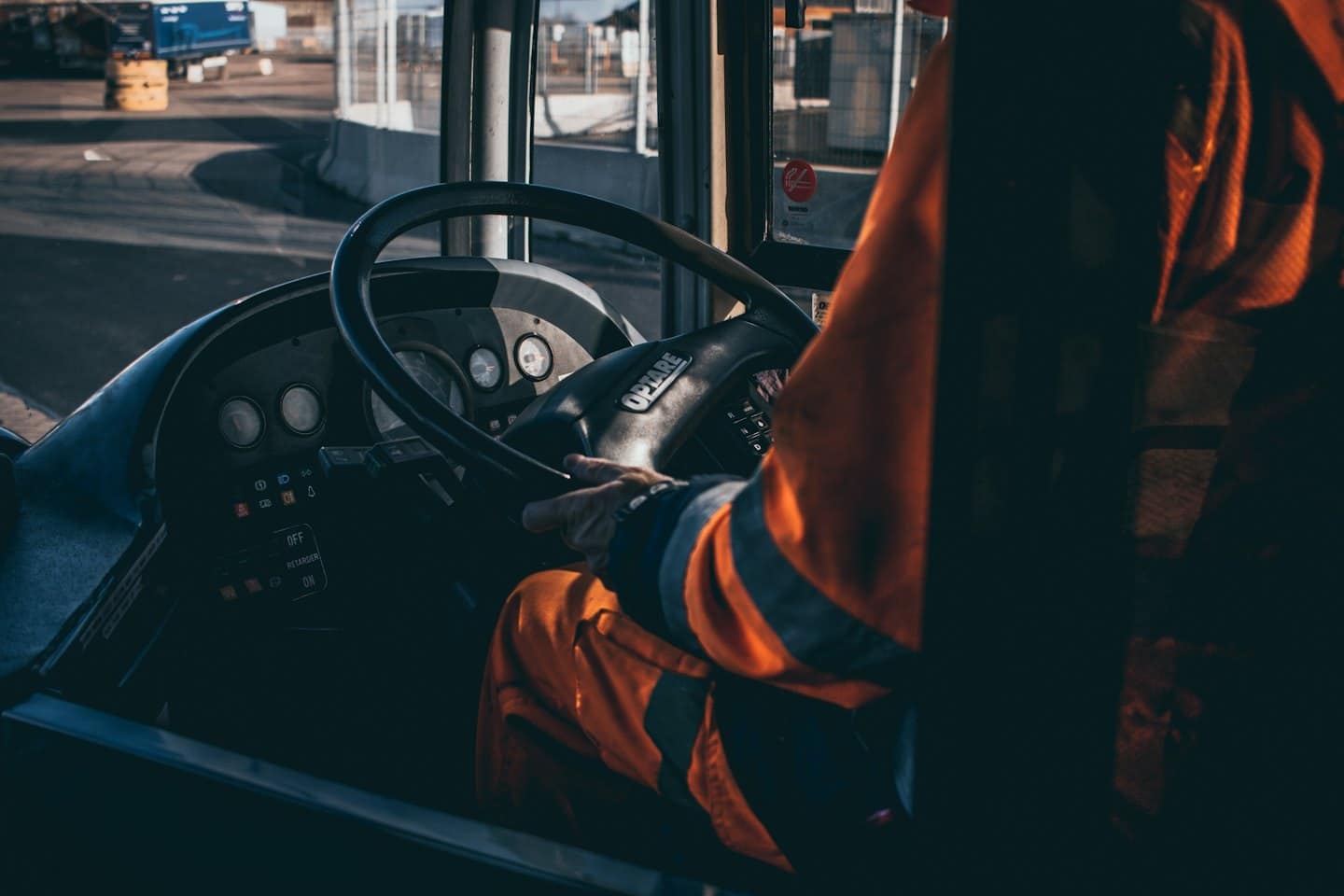 Autista in divisa arancione tiene il volante di un grosso veicolo.